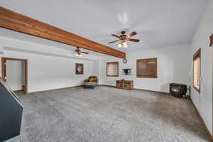 Unfurnished room with a wood stove, carpet flooring, a ceiling fan, and beam ceiling