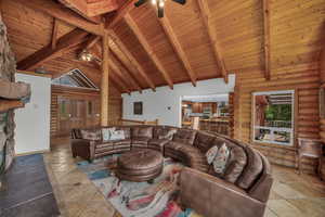 Living area featuring a ceiling fan, stone tile floors, healthy amount of natural light, a wooden ceiling with exposed beams, and high vaulted ceiling