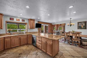 Kitchen featuring a textured ceiling, stone tile flooring, a peninsula, recessed lighting, and brown cabinets