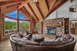 Living room with a wooden ceiling with exposed beams, stone tile flooring, log walls, a ceiling fan, and a stone fireplace