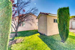View of side of property featuring stucco siding, a lawn, a tiled roof, and an outdoor structure