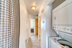Washroom featuring stacked washer and clothes dryer and light tile patterned floors