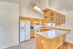 Kitchen featuring white appliances, a peninsula, glass insert cabinets, light countertops, and a breakfast bar area