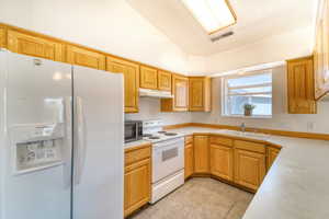 Kitchen featuring white appliances, light countertops, lofted ceiling, and under cabinet range hood