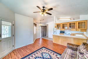 Kitchen featuring lofted ceiling, light wood finished floors, ceiling fan, white appliances, and glass insert cabinets