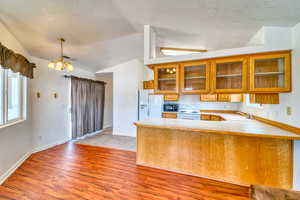 Kitchen with vaulted ceiling, a textured ceiling, brown cabinets, a chandelier, and light countertops
