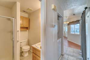 Bathroom featuring tile patterned floors, a stall shower, vanity, a chandelier, and washer and clothes dryer