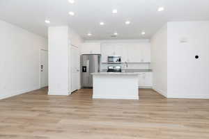 Kitchen with appliances with stainless steel finishes, an island with sink, white cabinetry, recessed lighting, and light wood-style floors