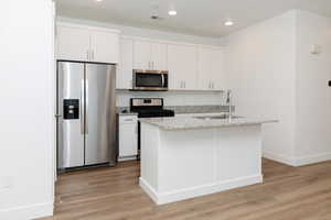 Kitchen featuring appliances with stainless steel finishes, white cabinets, light wood-style floors, a center island with sink, and recessed lighting