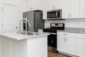 Kitchen with stainless steel appliances, white cabinets, wood finished floors, a kitchen island with sink, and light stone counters