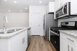 Kitchen with stainless steel appliances, light wood-style floors, white cabinetry, recessed lighting, and light stone counters