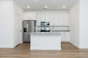 Kitchen with stainless steel appliances, white cabinets, light wood-style floors, a kitchen island with sink, and recessed lighting
