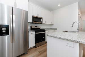 Kitchen with appliances with stainless steel finishes, light wood finished floors, white cabinetry, light stone counters, and recessed lighting