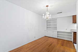 Unfurnished dining area with a chandelier, light wood-type flooring, and built in shelves