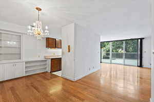 Unfurnished dining area with a chandelier, light wood finished floors, built in features, and a wall of windows