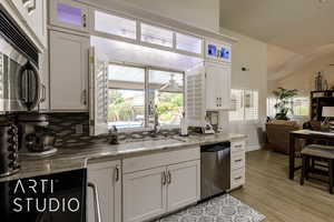 Kitchen featuring dishwasher, backsplash, light wood-style flooring, glass insert cabinets, and lofted ceiling