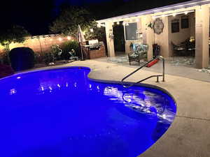 Pool at night featuring an outdoor kitchen and a patio