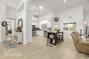 Kitchen featuring a high ceiling, open floor plan, white cabinetry, glass insert cabinets, and appliances with stainless steel finishes