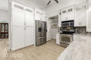 Kitchen with appliances with stainless steel finishes, a ceiling fan, light wood-type flooring, white cabinets, and decorative backsplash