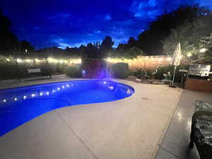 Pool at night featuring a patio area, a grill, and a fenced backyard