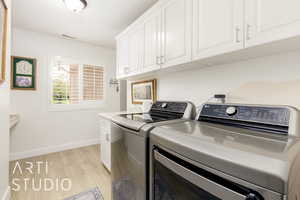 Laundry area featuring washing machine and dryer, light wood-style floors, and cabinet space
