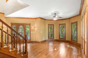 Entrance foyer with ornamental molding, stairway, wood finished floors, and a ceiling fan