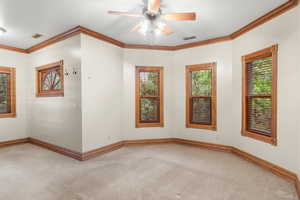 Carpeted spare room with crown molding and a ceiling fan