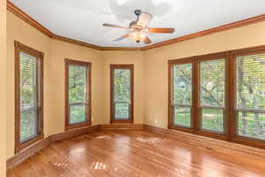 Spare room with ornamental molding, healthy amount of natural light, light wood-style flooring, and a ceiling fan