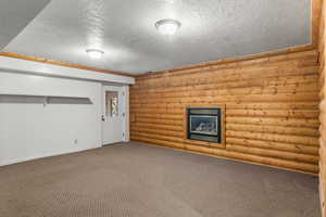 Unfurnished living room featuring log walls, carpet flooring, and a textured ceiling