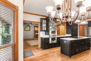 Kitchen featuring ornamental molding, a center island, appliances with stainless steel finishes, dark cabinets, and glass insert cabinets