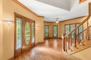 Foyer with ornamental molding, wood finished floors, stairway, and ceiling fan
