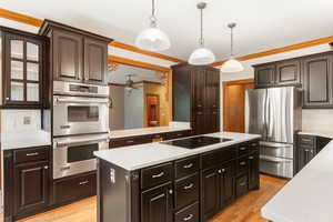 Kitchen featuring a kitchen island, stainless steel appliances, dark brown cabinetry, crown molding, and light wood finished floors