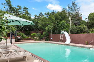 View of pool featuring a water slide, a fenced backyard, and view of scattered trees