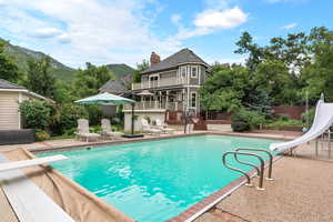 View of swimming pool with a water slide, a diving board, a patio, and a deck with mountain view