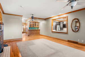 Unfurnished living room featuring ceiling fan, ornamental molding, and light wood finished floors