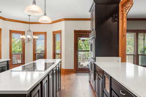 Kitchen with hanging light fixtures, dark brown cabinetry, ornamental molding, a kitchen island, and light stone countertops