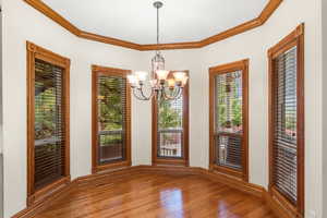 Unfurnished dining area with ornamental molding, wood finished floors, and a chandelier
