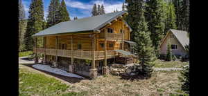 Rear view of house with a patio area, a metal roof, log exterior, stone siding, and a balcony