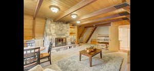 Living room with a wooden ceiling with exposed beams, a stone fireplace, stairway, and wooden walls