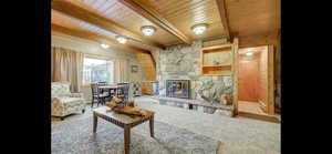 Carpeted living area featuring a wood ceiling with exposed beams, a stone fireplace, and baseboard heating