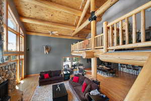 Living area with a wooden ceiling with exposed beams, a ceiling fan, wood finished floors, a stone fireplace, and high vaulted ceiling