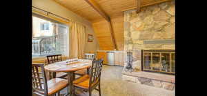 Dining space featuring wood ceiling, a stone fireplace, and carpet flooring