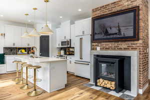 Kitchen with high end fridge, a center island with sink, light wood-style floors, recessed lighting, and a kitchen breakfast bar