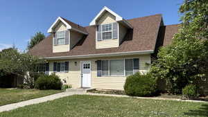 Cape cod home with a front yard and roof with shingles