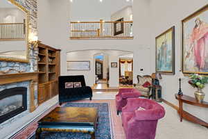 Living room featuring a stone fireplace, a high ceiling, arched walkways, and carpet flooring