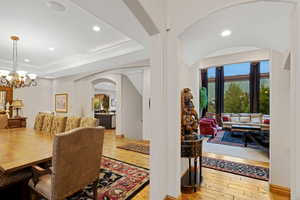 Dining area with arched walkways, light wood finished floors, recessed lighting, a chandelier, and a tray ceiling