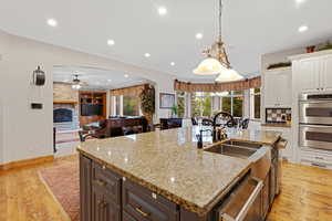 Kitchen with stainless steel appliances, light wood finished floors, decorative light fixtures, white cabinetry, and light stone countertops