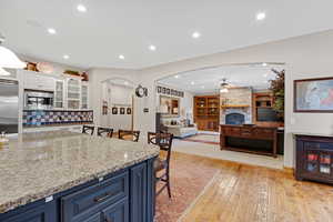 Kitchen with a kitchen bar, light stone countertops, blue cabinets, light wood finished floors, and arched walkways
