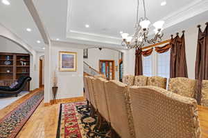 Dining space with arched walkways, recessed lighting, crown molding, light wood-style floors, and stairway