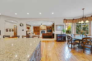 Kitchen featuring light stone countertops, a breakfast bar, a stone fireplace, light wood-style flooring, and recessed lighting
